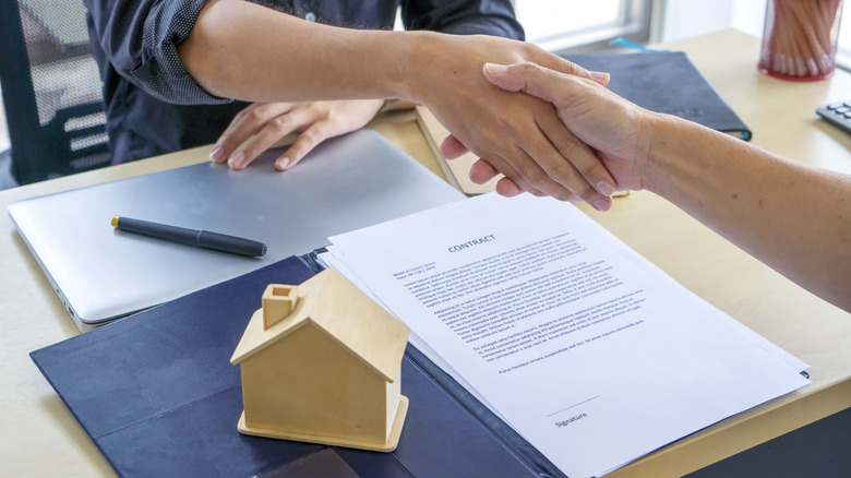Two people shake hands over a legal document related to real estate