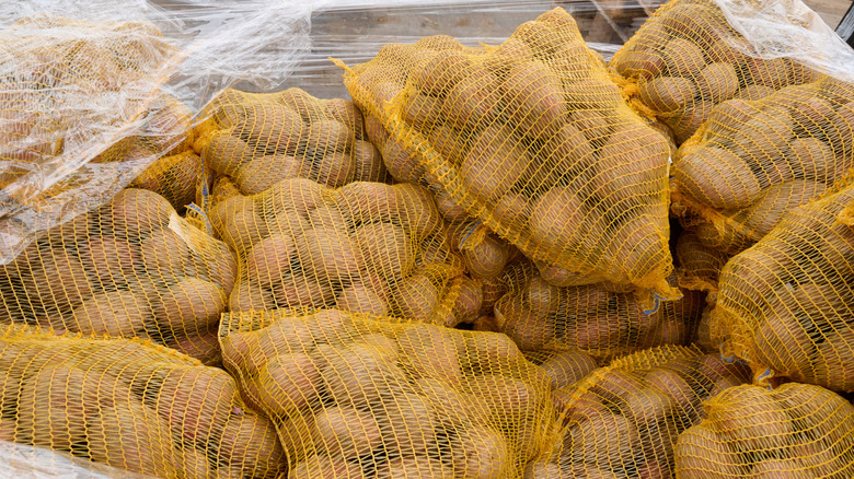 A pallet of potatoes is delivered to a grocery store with bundles separated into plastic mesh bags