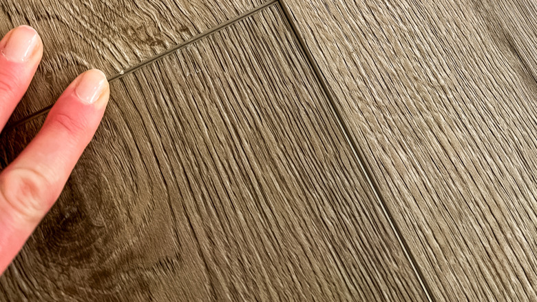 A hand pushes a loose vinyl plank into place