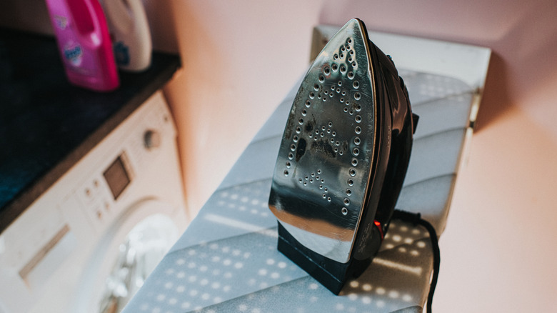 A black iron sits on an ironing board in a laundry room.