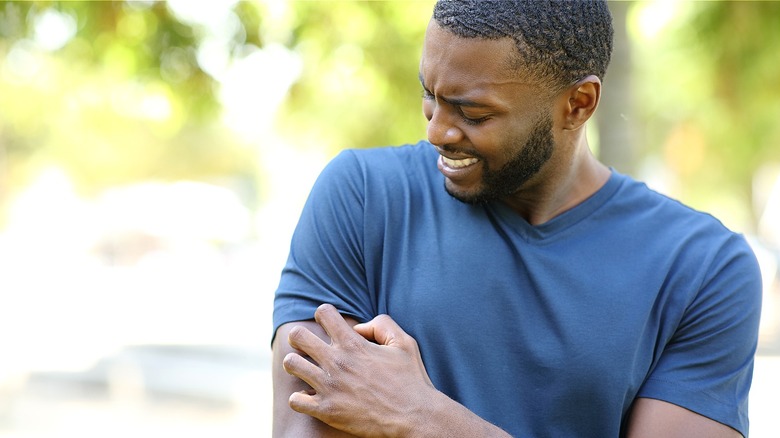 A person making a grimace while scratching at their arm while outside