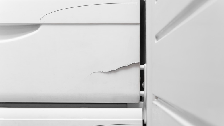 A plastic refrigerator drawer shelf with a large crack in it.