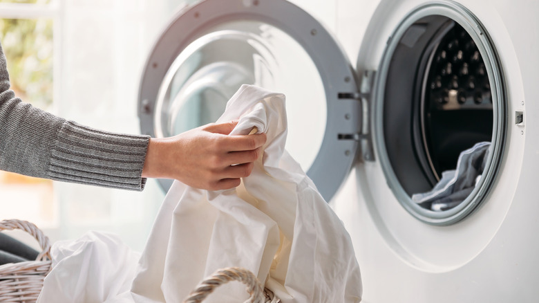 Close up of female hands dropping dirty laundry in the washing machine