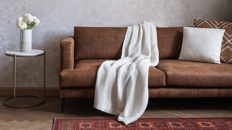 Leather couch with throw and pillows in front of a gray wall