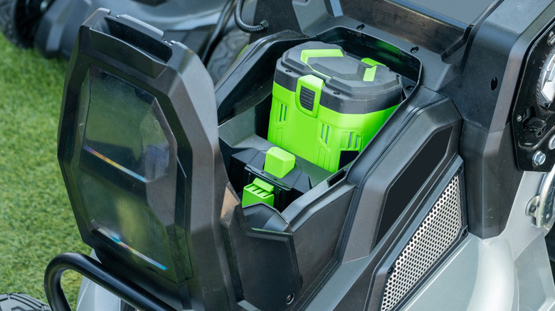 A grey and silver battery operated eco lawnmower with an open lid and a bright green battery.