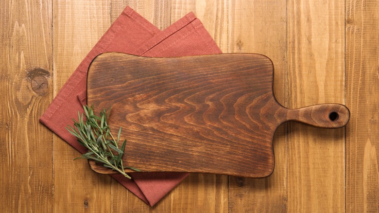 a rustic cutting board on a red napkin with a sprig of rosemary