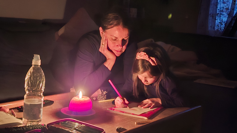 Young girl drawing a picture on paper by candlelight during power outage