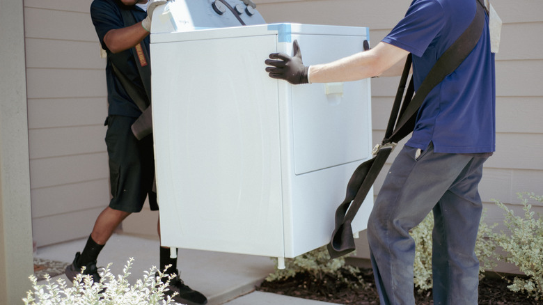 Two people moving a white washing machine.