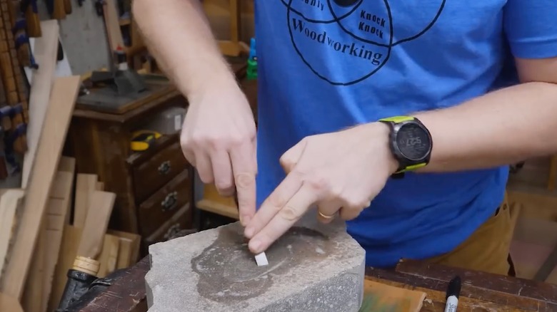 A man sharpening a chisel on a concrete block