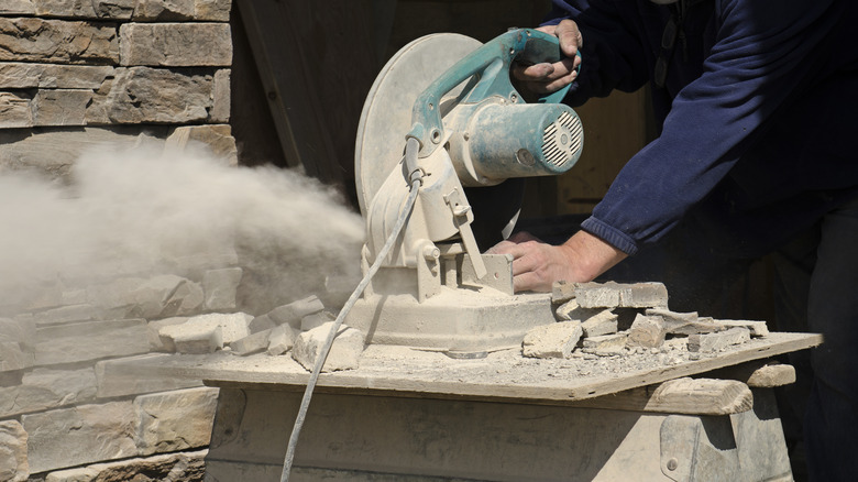 A cloud of dust is kicked up by a dry circular saw cutting pavers