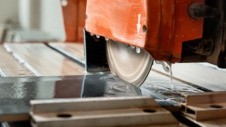 The diamond blade of a wet saw cuts through a thin paver