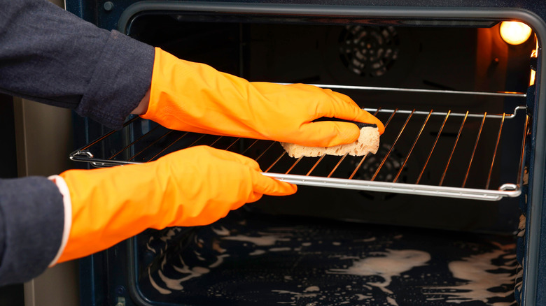 Someone wearing gloves and cleaning an oven grate with a sponge