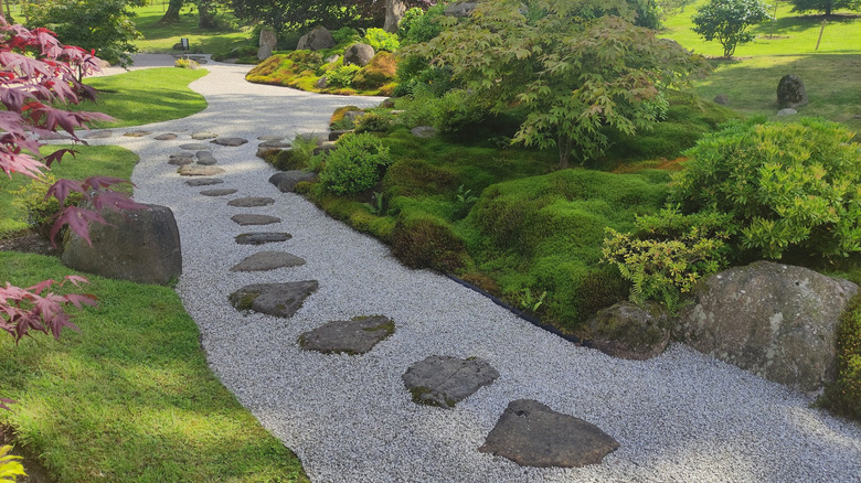 Garden pathway of gravel and stepping stones lined with mossy rocks and foliage.