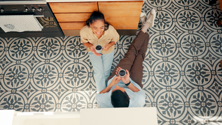 happy couple drinking coffee sitting on tile floor in kitchen