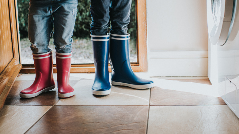 close up on two people in rain boots standing in open door way on checkered tiled floor