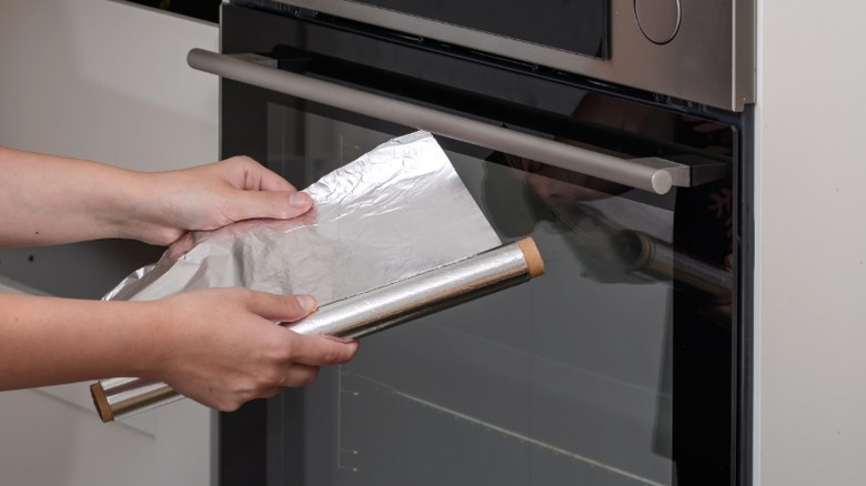 Person unrolling aluminum foil in front of oven