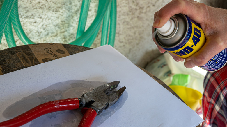 Hand spraying WD-40 onto pliers
