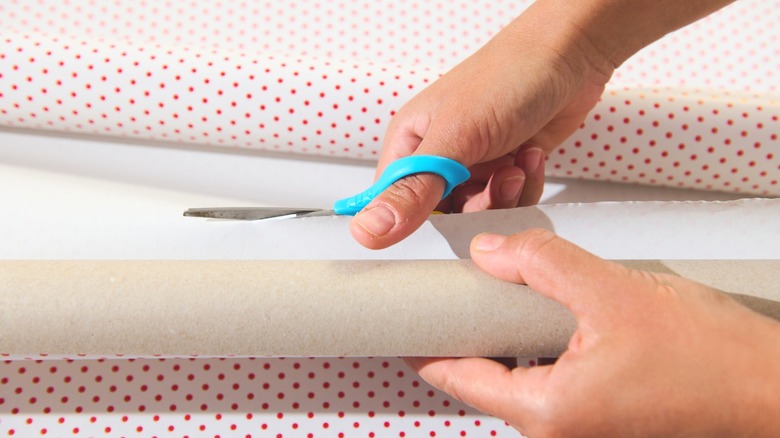 Person cutting through polka dotted wrapping paper with blue-handled scissors