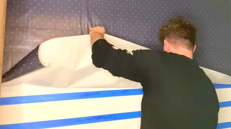 Man installing blue polka dot wrapping paper as wallpaper over strips of blue tape