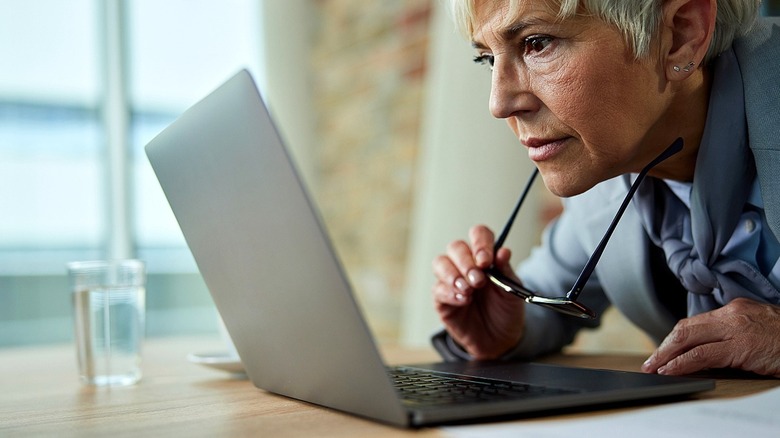 A person takes their glasses off to look more closely at their laptop screen