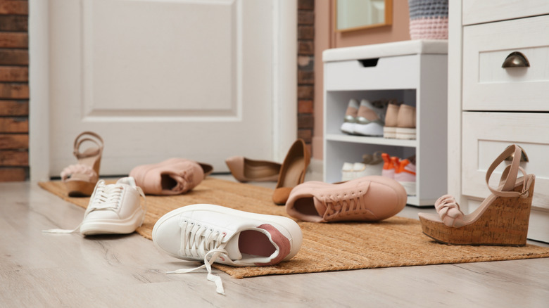 A cluttered pile of shoes around a shoe rack
