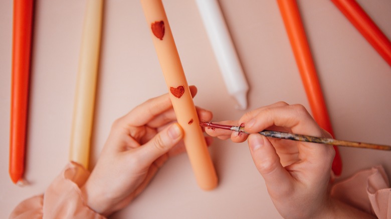 person painting hearts on tapered candle