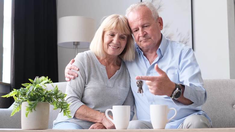 Senior couple sits on couch looking at set of keys dangling from man's finger