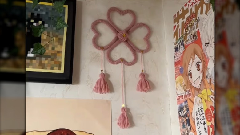 A wall hanging made from yarn-wrapped hearts hangs on a wall.