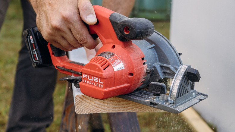 A male hand is using a Milwaukee saw to cut wood