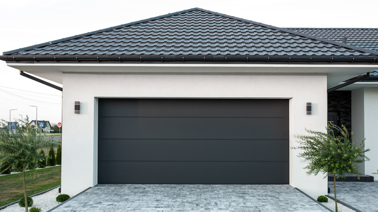 White garage with black roof and black door attached to a house