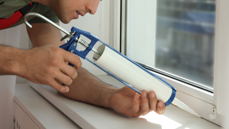 man caulking window inside 