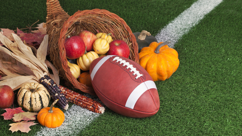 Cornucopia on football field holding apples, corn, gourds, leaves, and a football