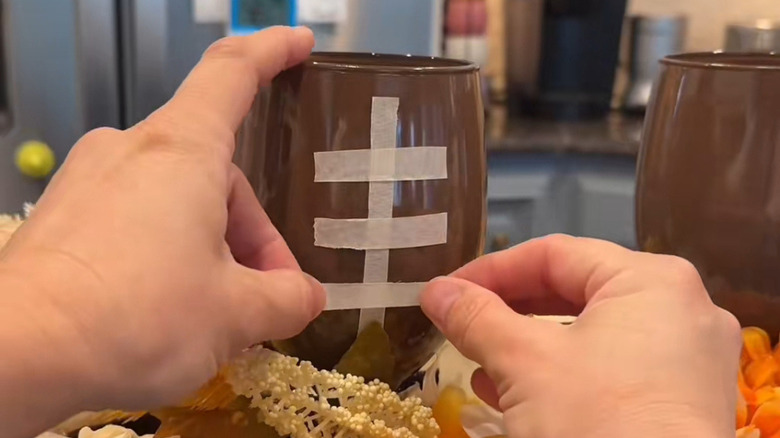 Hands placing tape on brown wine glass to mimic football