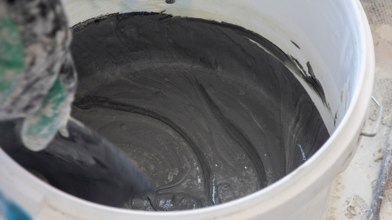 A person prepares microcement mixture in plastic bucket
