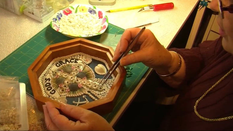 Woman making sailors' valentine with white seashells.