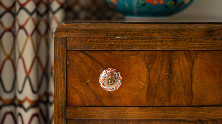 A colorful ceramic knob on a wooden chest of drawers