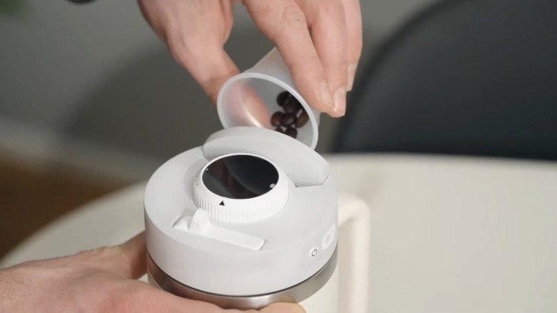 Person pouring whole coffee beans into Ecoldbrew coffee maker-cup combo