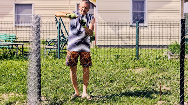 A man installs a chain link fence at a home