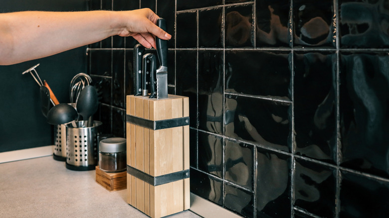 A person pulls a serrated knife out of their clean kitchen knife block.