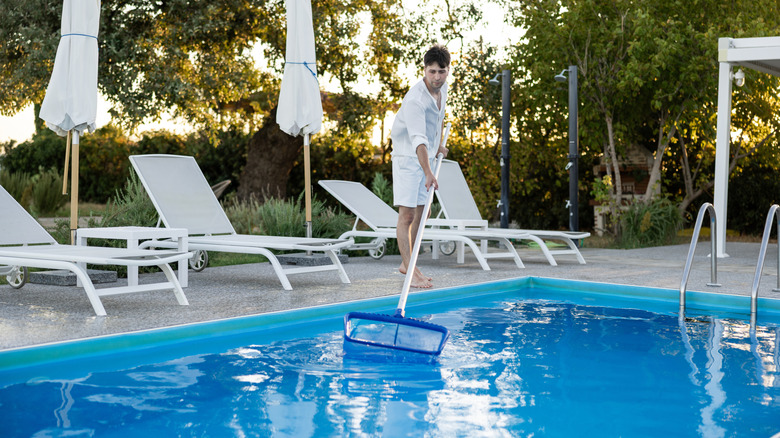 A man in a white outfit using a large net to pull items off the surface of the water