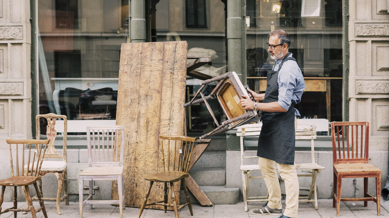 A man lifting up a vintage chair outside a shop.