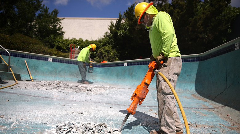Construction workers demolish a swimming pool.