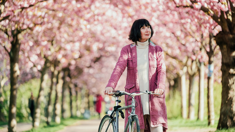 A woman walks down a path of cherry blossom trees and admires the sight