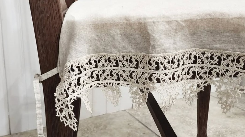 A wood dining chair with a white lace and linen cover