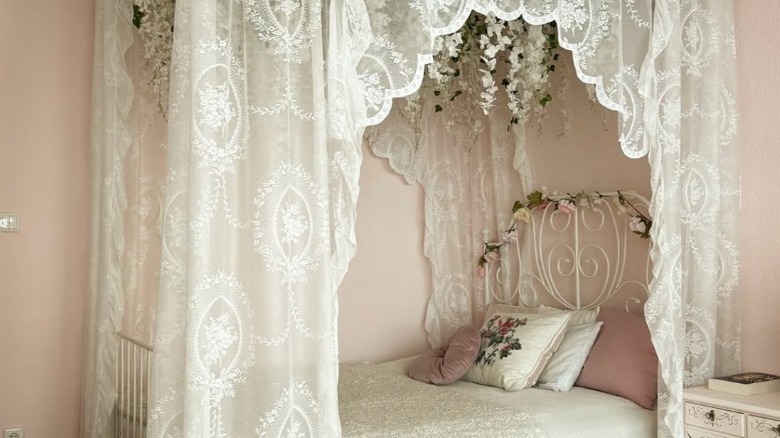 A pink and white bed with a lace canopy along the top