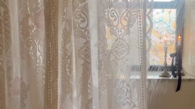 A lace curtain used as a shower curtain in a white bathroom