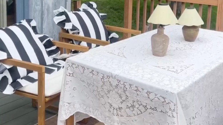 An outdoor table with a white lace tablecloth and two lamps
