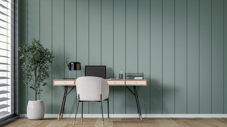 Minimalist (Scandinavian) home office interior with a modern desk, unique white chair, and potted plant next to a large window with blinds.