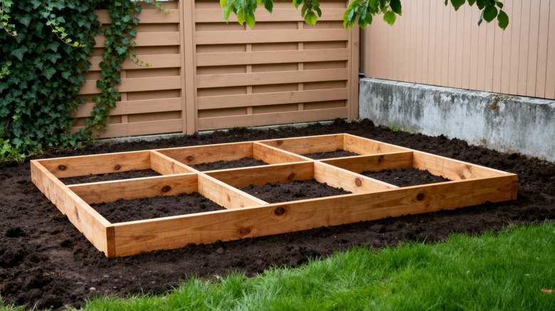 A wooden frame for a raised garden bed sits on freshly turned over soil.