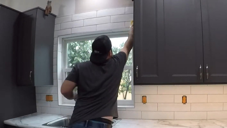 A small window behind the sink wedged between cabinets with white tile all around it